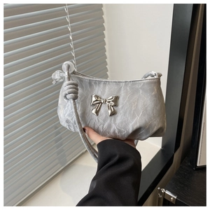 Detailed view of silver pleated shoulder bag with metallic bow and knotted strap texture