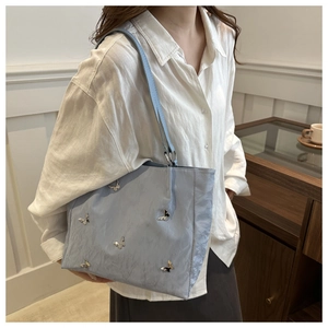 Close-up of light blue textured bucket bag with metallic butterfly accents and shoulder strap