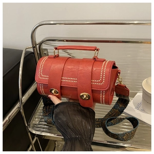 Detail of red cylinder bag featuring gold rivets and ethnic woven wide shoulder strap