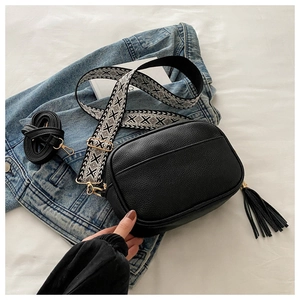 Dettaglio borsa a tracolla nera con tracolla etnica geometrica e nappa su denim