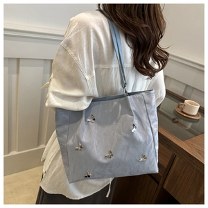 Macro view of light blue fabric bucket bag with delicate silver butterfly metal accents