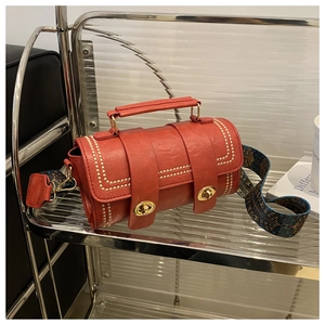Close-up of red cylindrical bag with gold rivet edges and dual metallic twist locks