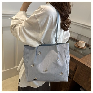 Close-up of light blue pleated bucket bag with silver butterfly charms and shoulder strap