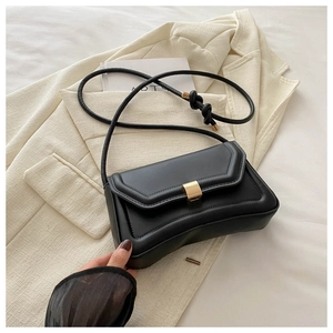 Detail view of black minimalist saddle bag with gold buckle and knotted shoulder strap