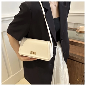 Detail of a white crossbody bag with gold rectangular clasp on a seated model