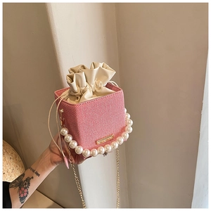 Détail du sac seau tissé rose avec poignée en perles et bandoulière chaîne dorée
