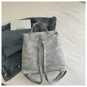 Flat lay of a metallic silver pleated backpack with denim jacket and minimalist art book