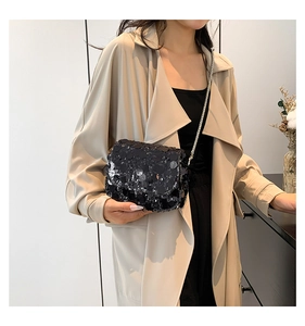 Detail of a black sequin crossbody bag with a slim silver chain strap on a model