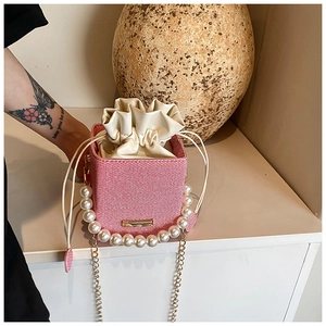 Détail du sac seau tissé avec poignée en perles et bandoulière en chaîne dorée