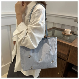 Detail of light blue bucket bag featuring silver butterfly accents and pleated texture