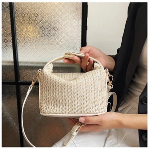 Detail of cream woven straw handbag with gold clasp and leather trim held by model