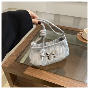 Detail of silver pleated handbag with metal bow and clear beads on a glass table