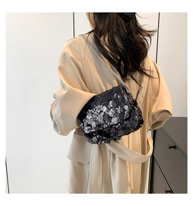 Close-up of black sequined shoulder bag with silver chain worn over a beige coat