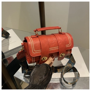 Close-up of red cylinder handbag with gold hardware and ethnic style printed strap