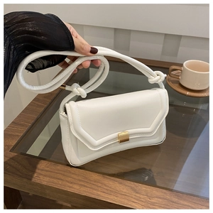 Close-up of white minimalist saddle bag with gold clasp and knotted rope strap