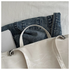 Detail of white textured leather tote with silver metal eyelets and soft chain strap