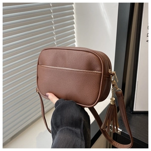 Dettaglio borsa a tracolla in pelle marrone con motivo litchi e cerniera con nappa decorativa