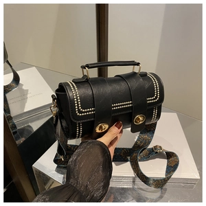 Detail of black faux leather pillow bag with gold studs and ethnic patterned strap