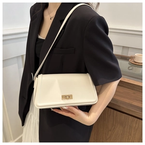 Detail of a white leather shoulder bag with a gold lock worn over a black blazer