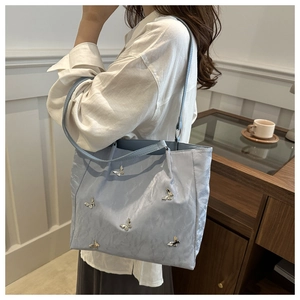 Detail of light blue tote bag with silver butterfly charms worn by a model in soft light