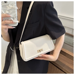 White minimalist shoulder bag with gold rectangular clasp shown on model in office setting
