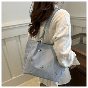 Detail of light blue bucket bag with silver metal butterflies on a textured surface