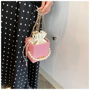 Détail du sac boîte tissé rose avec poignée en perles et bandoulière en chaîne dorée