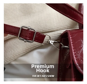 Close-up of silver metal hook and adjustable strap on burgundy patent leather bag