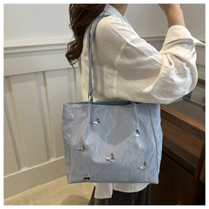 Detailed view of light blue pleated tote bag with golden butterfly charms and double straps