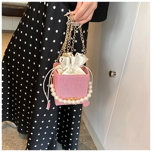 Pink woven box bag with oversized pearl handle and gold chain detail on floral dress