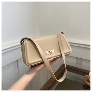 Close-up of a chic beige baguette bag with gold buckle being held against a white wall