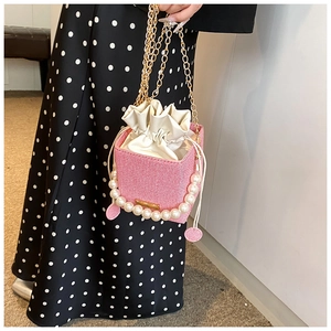 Détail d'un sac seau rose tressé avec poignée en perles et bandoulière dorée
