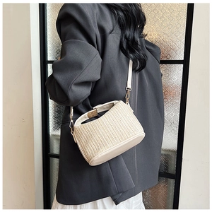 Detail of beige woven straw bag featuring leather base and elegant metal hook hardware