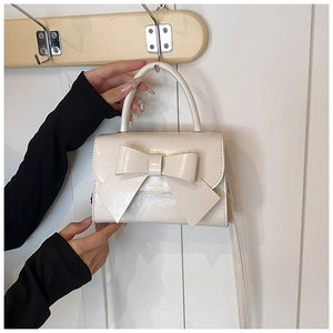 Detail of a creamy white bow handbag featuring glossy faux leather and fine texture