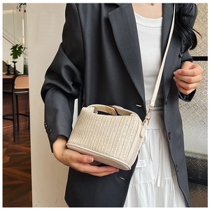 Detail of handwoven straw crossbody bag with cream leather trim and gold metal hooks