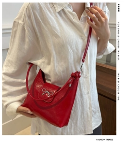 Détail du sac rouge brillant avec nœud argenté et bandoulière à nœuds ajustable