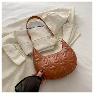 Close-up of brown crescent underarm bag with geometric quilted texture on white blazer