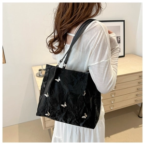 Detail of black textured bucket bag featuring silver 3D butterfly embellishments