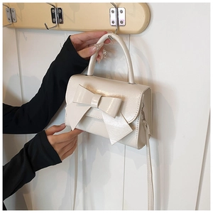 Detail of a creamy white bow handbag with glossy texture and pleated leather finish