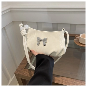 Close-up of cream shoulder bag featuring silver bow detail and elegant pearl accents