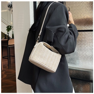 Close-up of minimalist beige woven straw crossbody bag with leather strap on a model