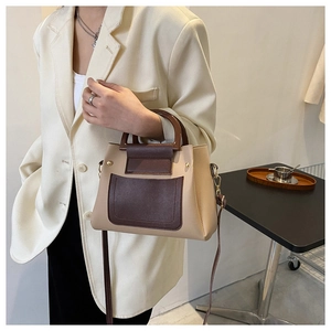 Model showcasing a beige and dark brown leather crossbody bag with top handle and golden hardware
