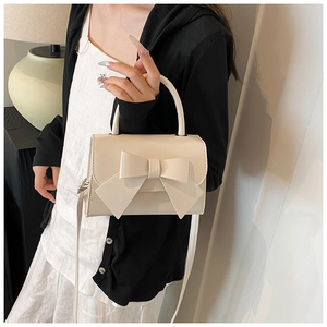 Detail of a chic cream handbag featuring a large bow and soft PU leather texture