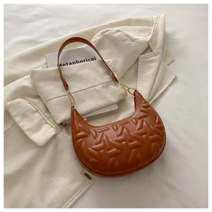 Close-up of caramel crescent bag featuring geometric embossed texture and gold ring