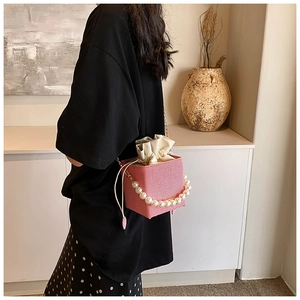 Pink cube bucket bag with pearl handle and metal chain strap in modern interior setting