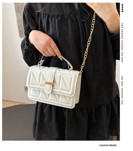 Detail of white quilted crossbody bag with golden H-clasp and metal chain strap
