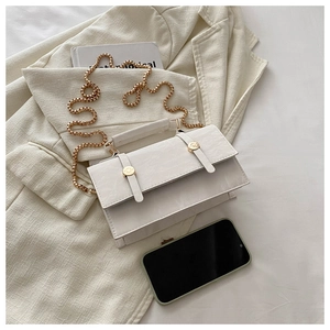 Top view of white textured leather crossbody bag with chunky gold chain on a beige blazer
