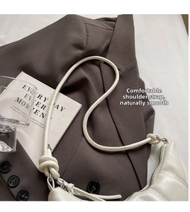 Detail of creamy white quilted moon bag with knotted strap on a brown blazer background