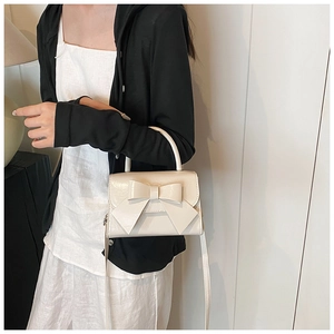 Detail view of cream bow handbag showing shiny leather texture and stylish crossbody strap