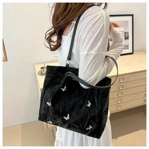 Detail of black bucket bag featuring crinkled texture and silver butterfly embellishments